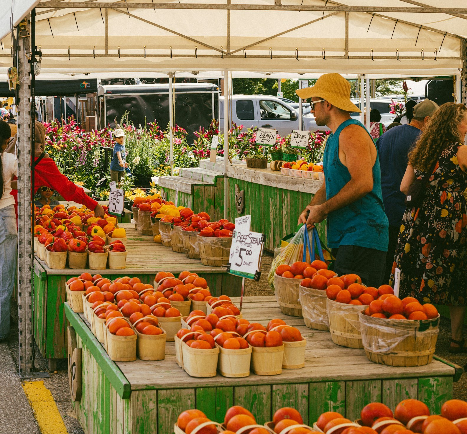 Bushel baskets of fresh tomatoes and peppers for sale at an outdoor farmers market stall.